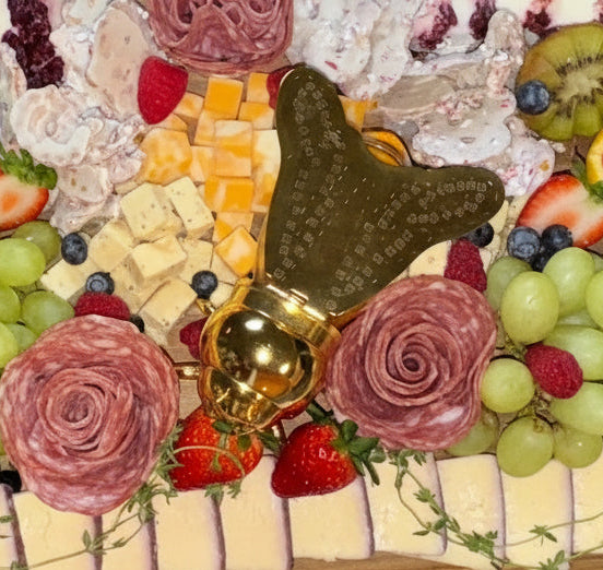 Decorative charcuterie board with fruits, meats, and flowers on a marble surface